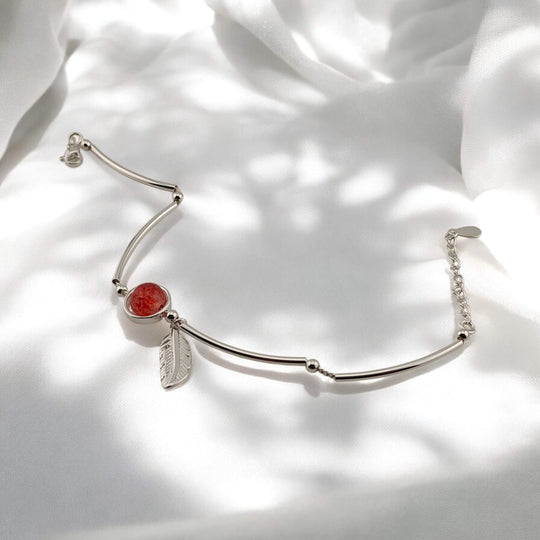 Open silver bracelet with red center charm and feather accent