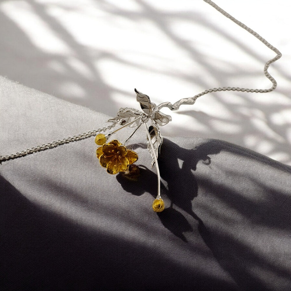 White-gold necklace with gold blossom pendant displayed on a gray fabric surface

