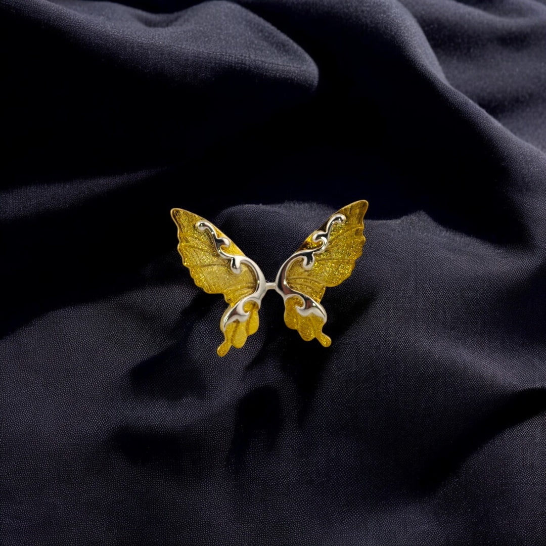 Close-up of a gold butterfly wing ring on black fabric

