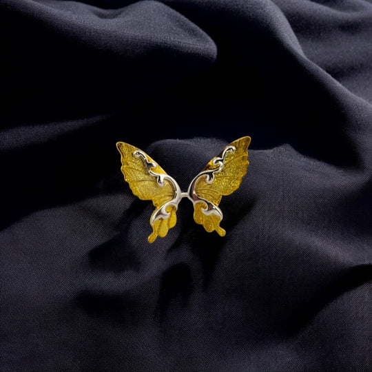Close-up of a gold butterfly wing ring on black fabric

