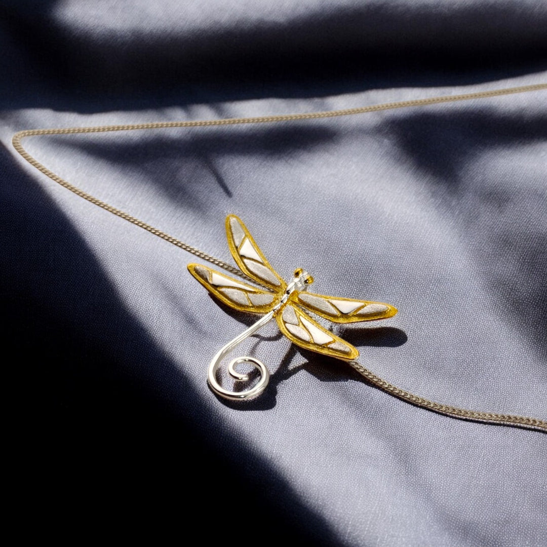 Minimalist golden dragonfly necklace centered on dark silky fabric.

