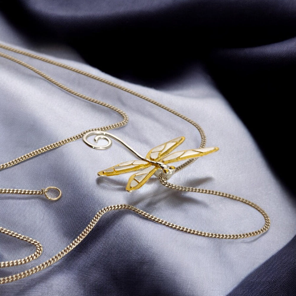Detailed view of white-gold chain and golden dragonfly pendant in soft lighting.

