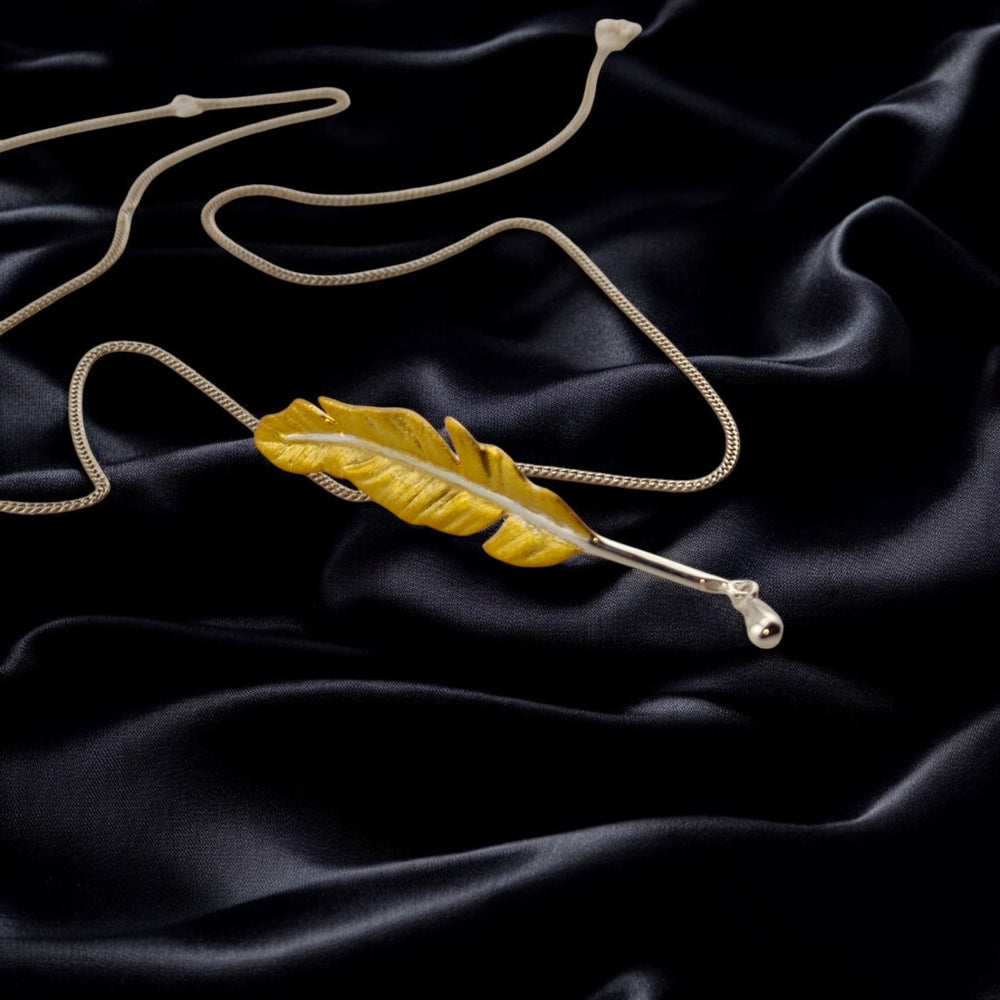gold feather pendant with white-gold chain centered on black satin