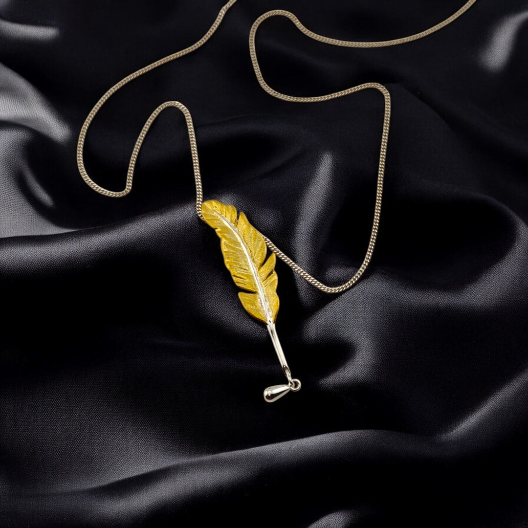 gold feather pendant with white-gold chain artistically arranged on black fabric