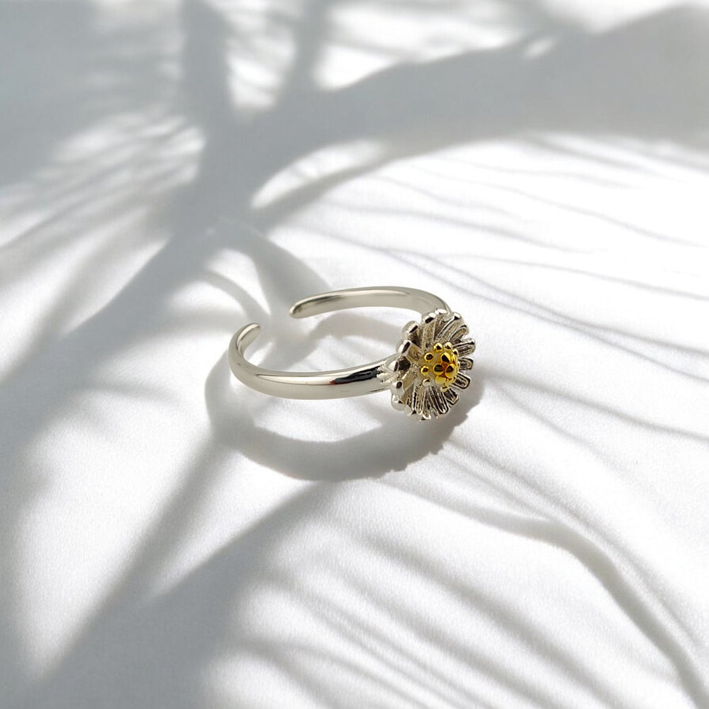 Silver sunflower ring with gold-plated center on white fabric with leaf shadows