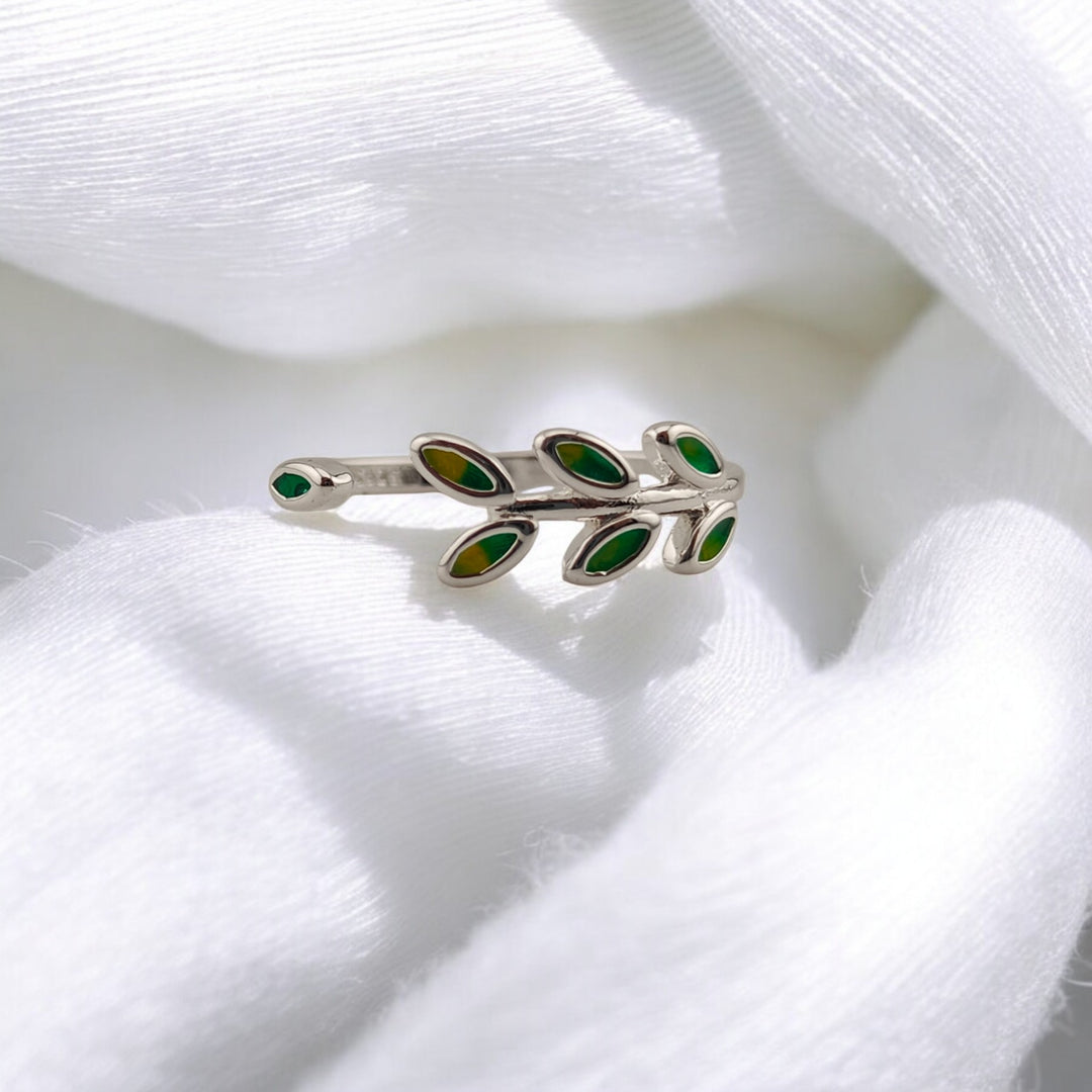 Silver botanical ring with vibrant green leaf design on fabric