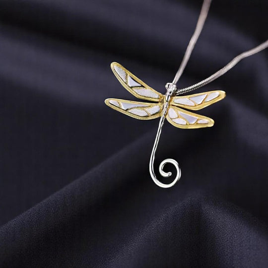Elegant dragonfly necklace in white-gold and gold tones resting softly on fabric.

