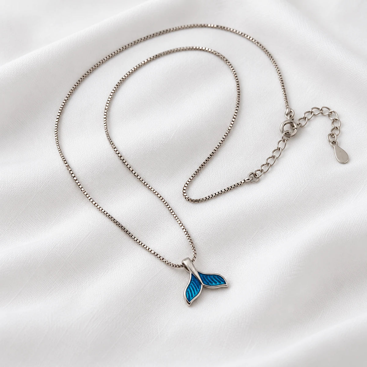 Blue dolphin tail pendant on a silver-tone necklace laid on white fabric