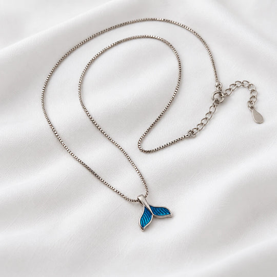 Blue dolphin tail pendant on a silver-tone necklace laid on white fabric