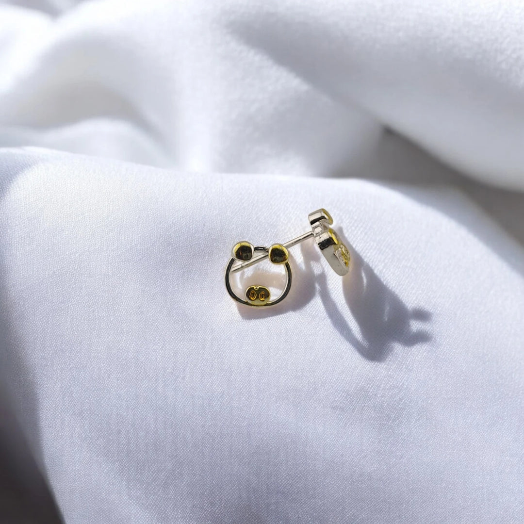 Angled view of the two-tone pig stud earrings with butterfly backs