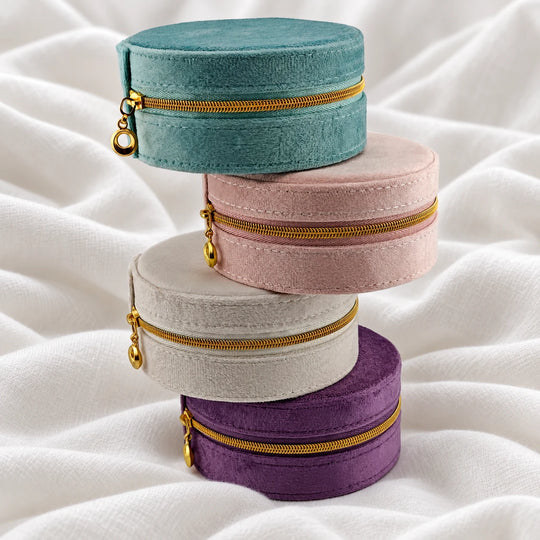 Round velvet jewelry cases stacked in teal, pink, cream and purple with gold-tone zippers